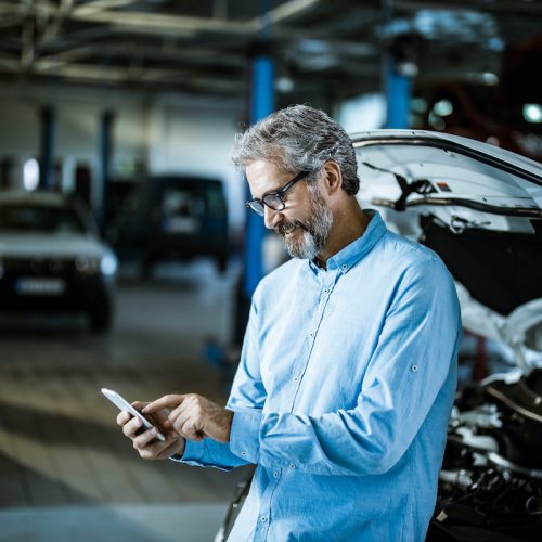 Happy inspector using mobile phone in auto repair shop.