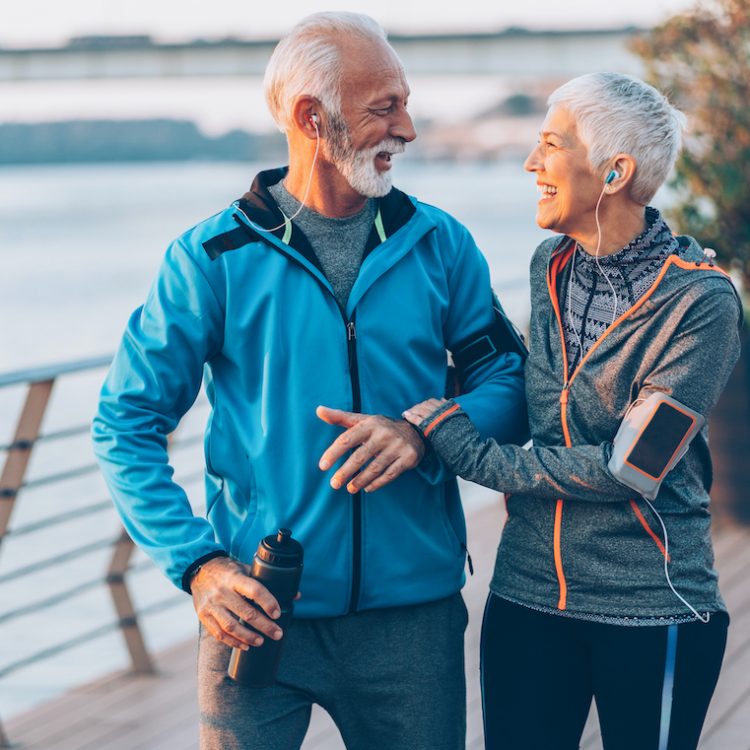 Senior couple in sports clothing and sports technologies jogging together across the bridge